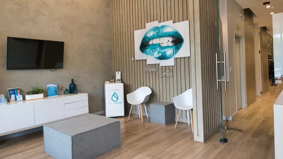 Waiting area at Meadowbrook Dentistry in Plainview, NY, with teal smile artwork, white chairs, and a hallway to the treatment rooms