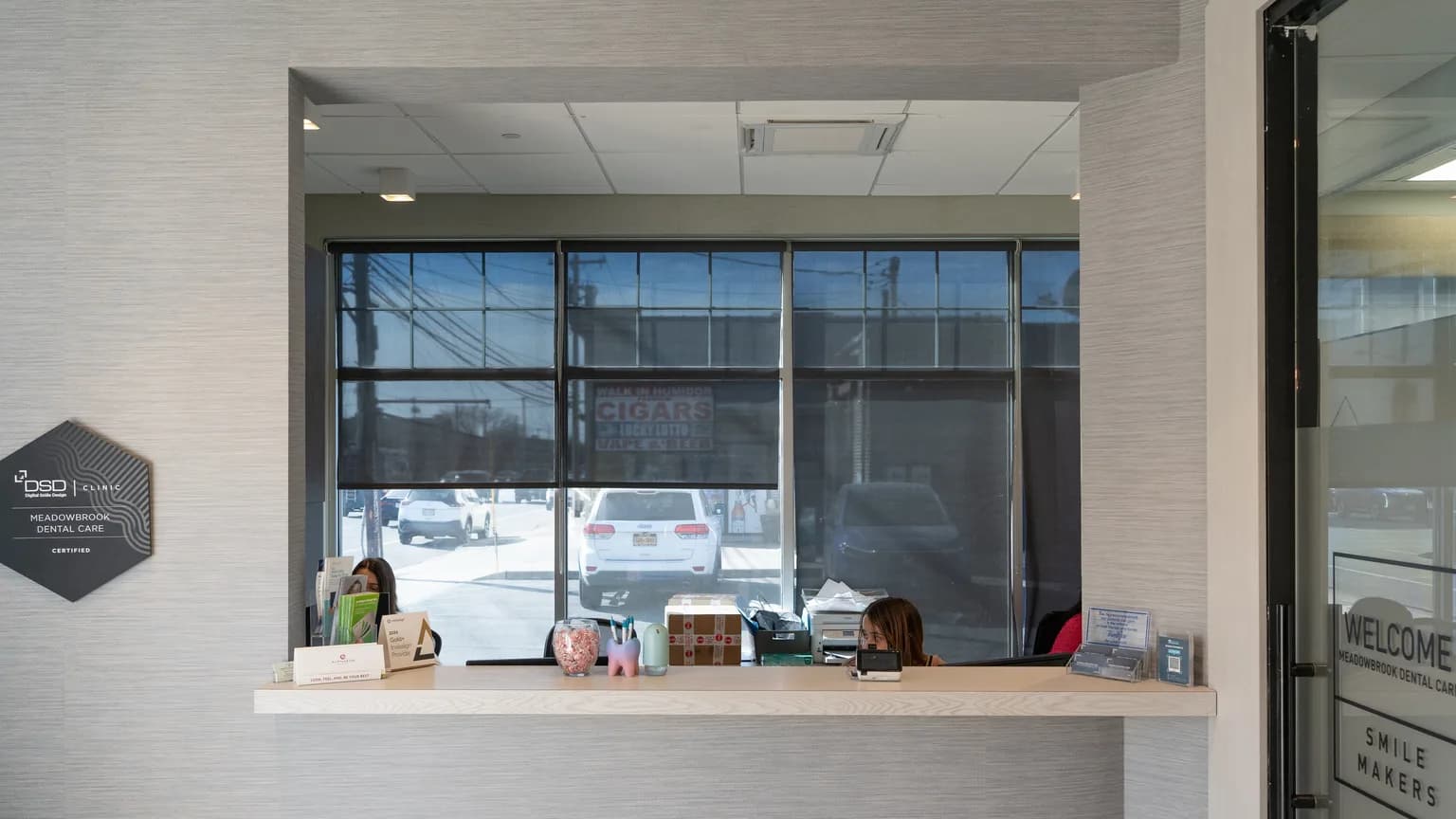 Front desk and reception area inside the Meadowbrook Dental Care office in Mineola, with a welcome sign on the glass entry door