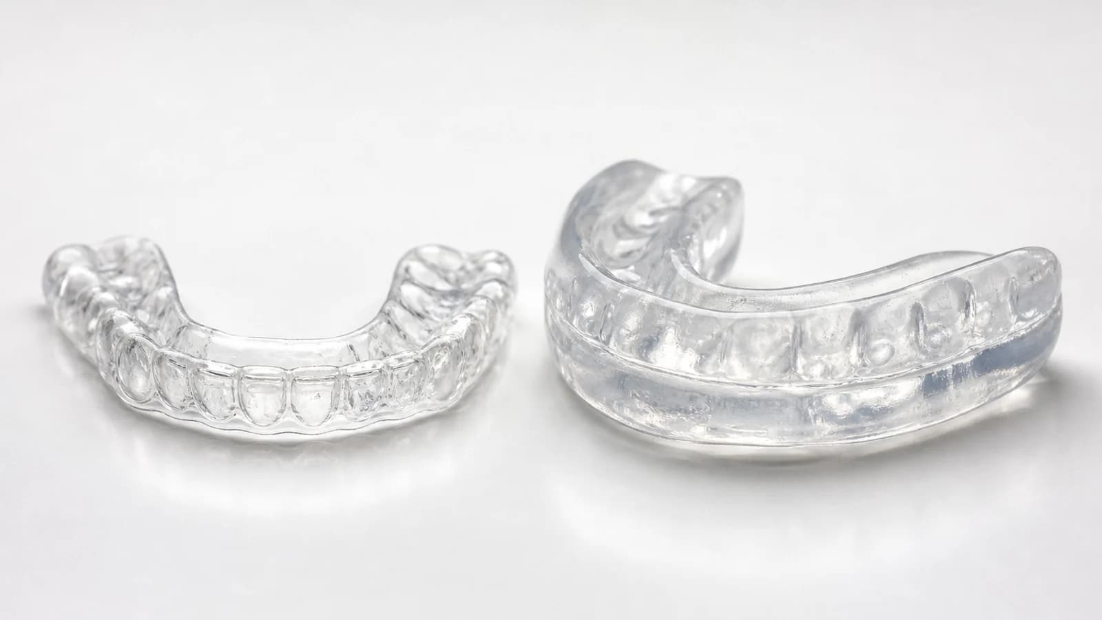 A close-up comparison of a slim clear custom night guard next to a bulkier generic boil-and-bite mouth guard on a clean surface