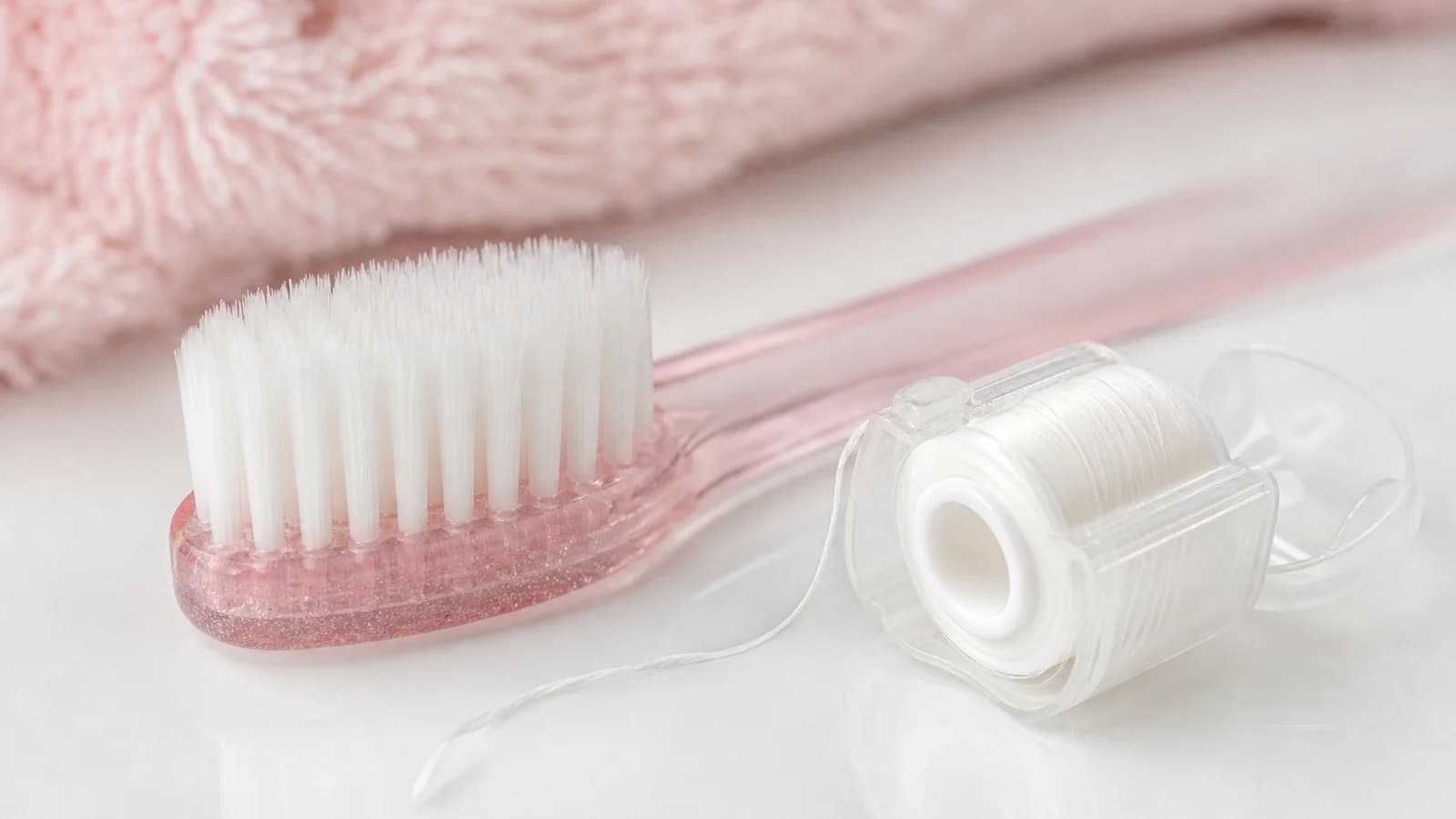 A close-up of a soft-bristled toothbrush and dental floss on a white surface, representing gentle gum care
